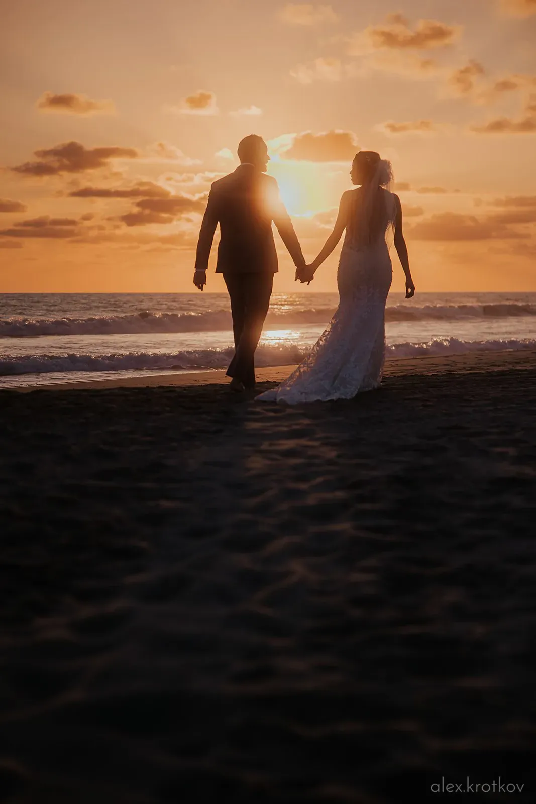 Married couple hold hands facing a sunset